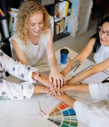 Diverse colleagues uniting hands together over color palette at the workplace, symbolizing teamwork.